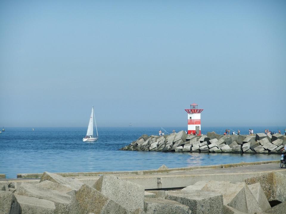 Segelboot vor Leuchtturm und Mole an der Nordsee