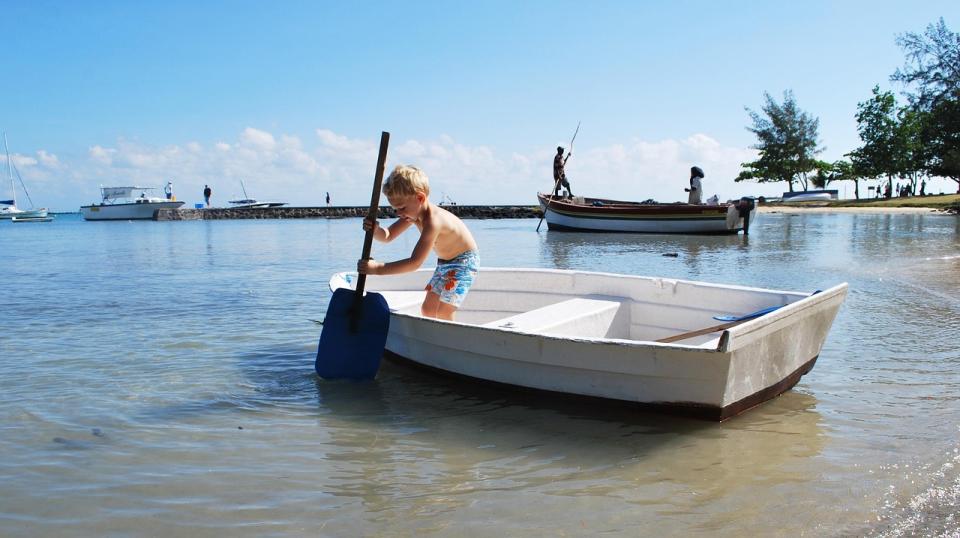 Kind schiebt ein Ruderboot durch flaches, klares Wasser